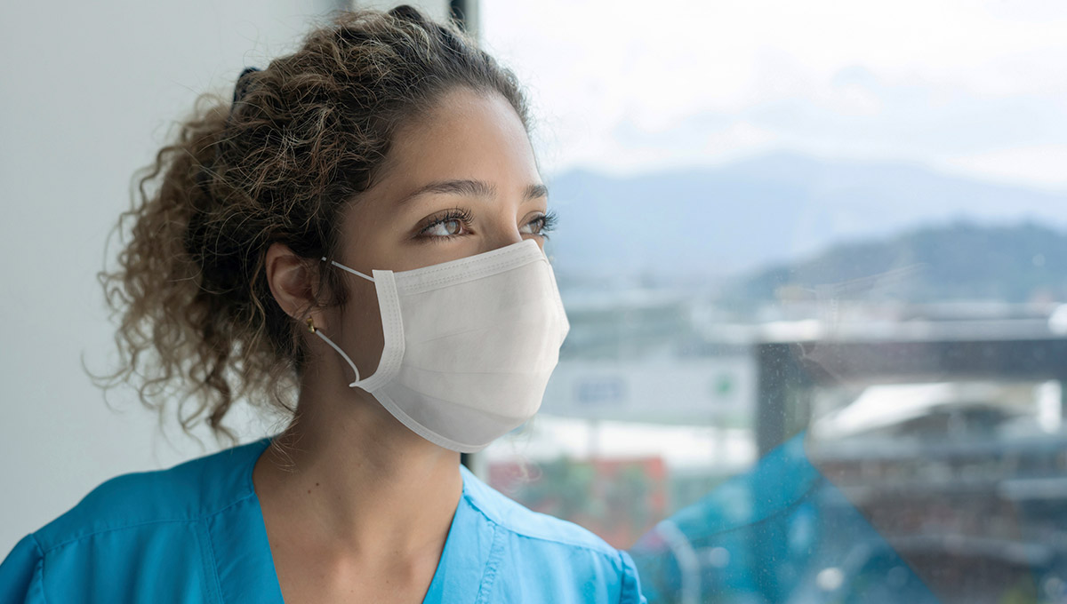 Healthcare nurse looking into the distance with a mask on her face outside of a hospital