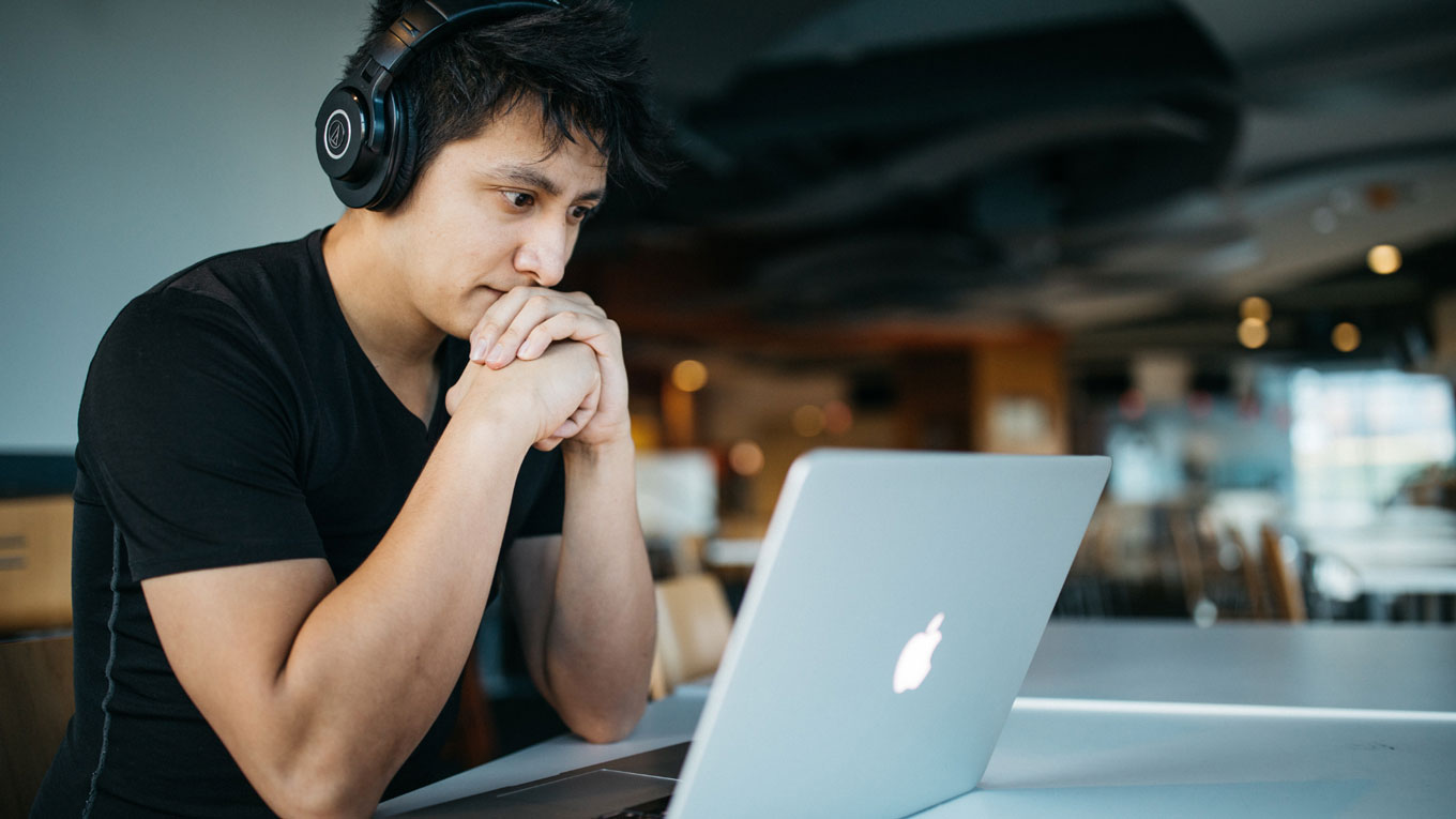 young man concentrates looking at laptop with headphones on