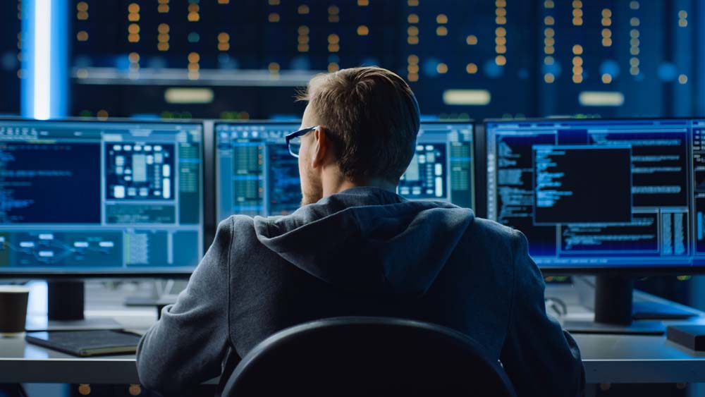 BigBear.ai AI Softwares and Solutions for Department of Defense and Government. Image featuring IT Specialist Working on Personal Computer with Monitors Showing Coding Language Program. Technical Room of Data Center with Server Rack.