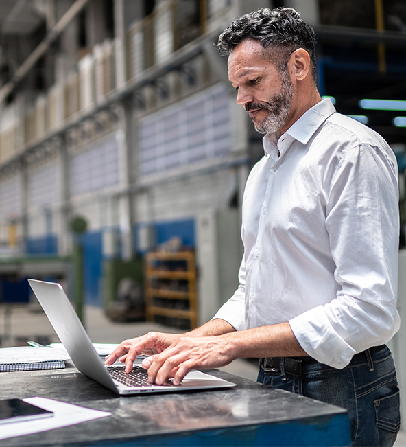 business man stands in warehouse at laptop computer